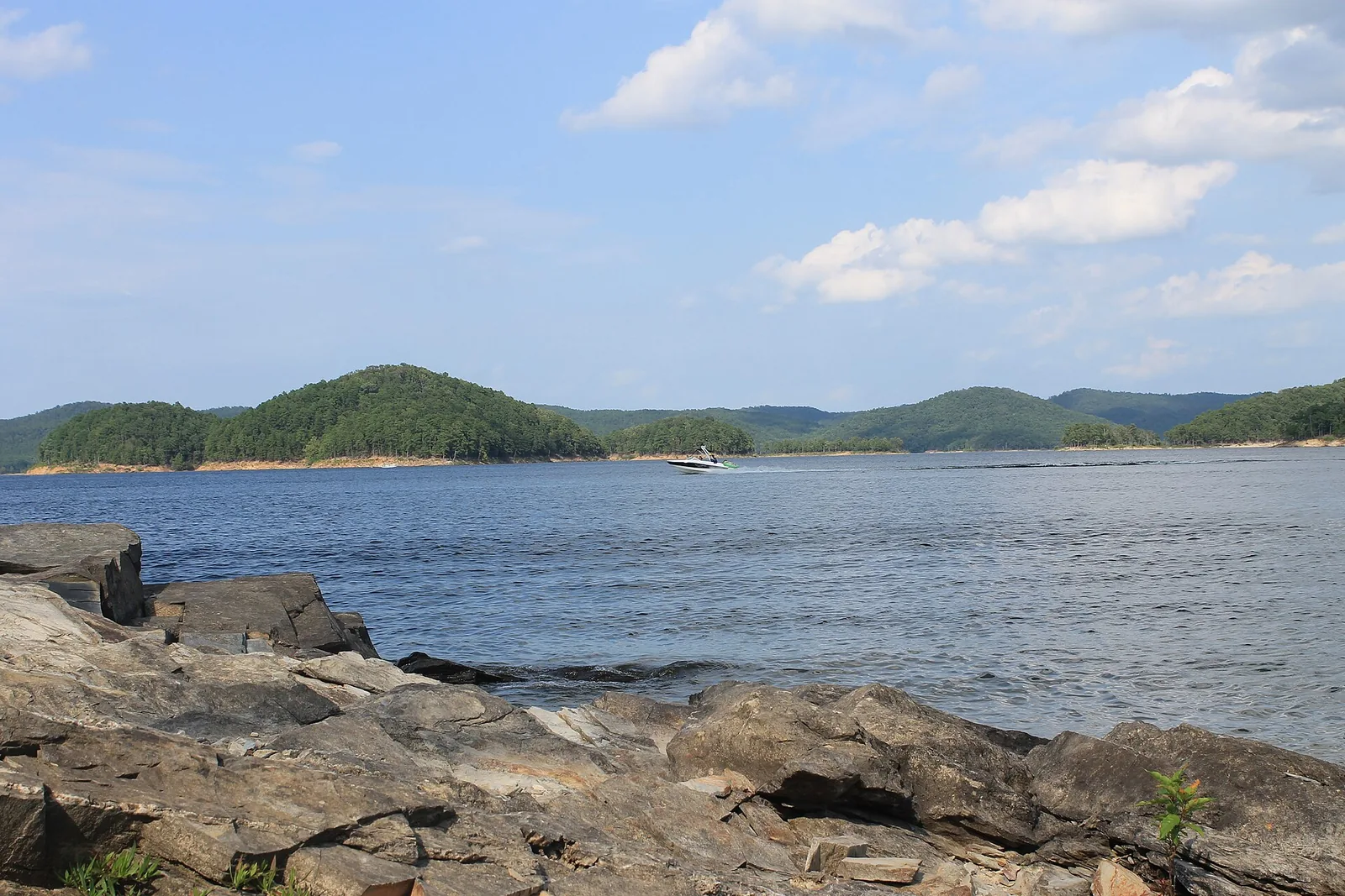 Boating on the clear water of Broken Bow Lake with forested hills behind