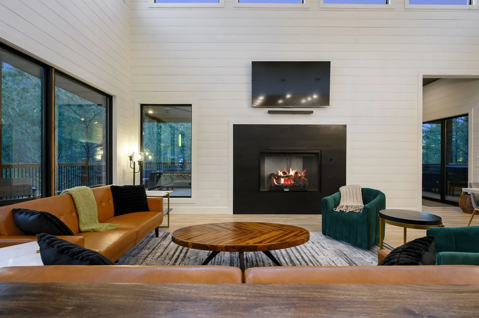 Living room at The Arcadia with camel leather sofas, emerald green chairs, linear fireplace, and shiplap walls