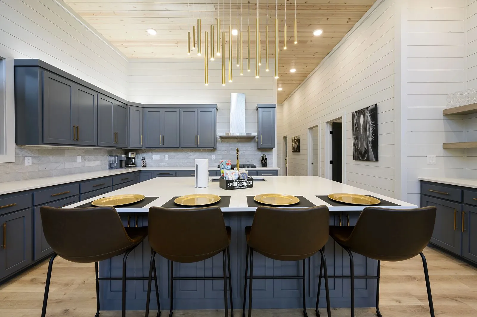 Kitchen island at The Arcadia with bar stools, gray cabinetry, and vaulted wood ceiling with pendant lights