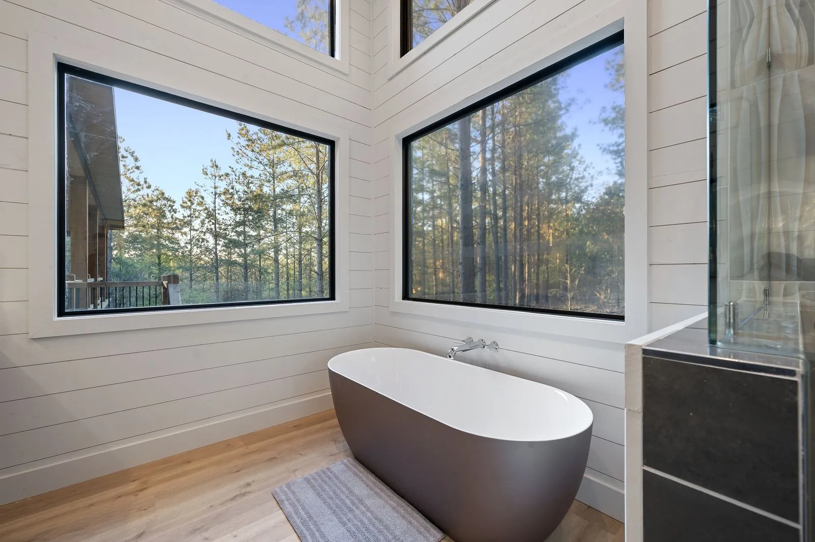 Primary bathroom at The Arcadia with freestanding dark soaking tub, forest-view windows, and glass shower