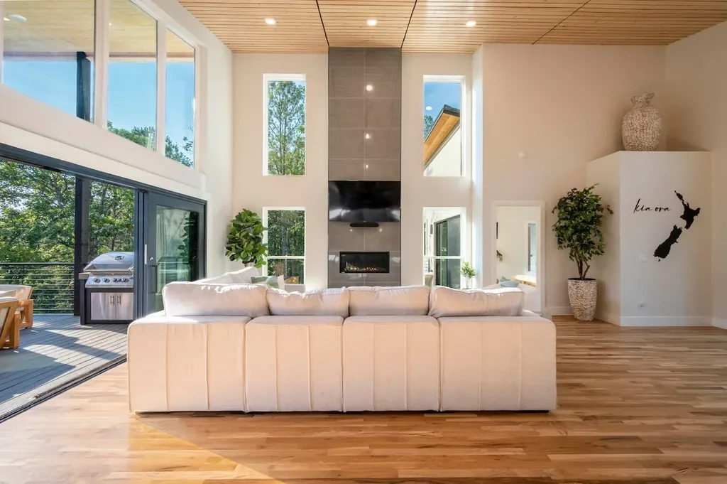 Double-height living room with fireplace and forest windows at The Aroha
