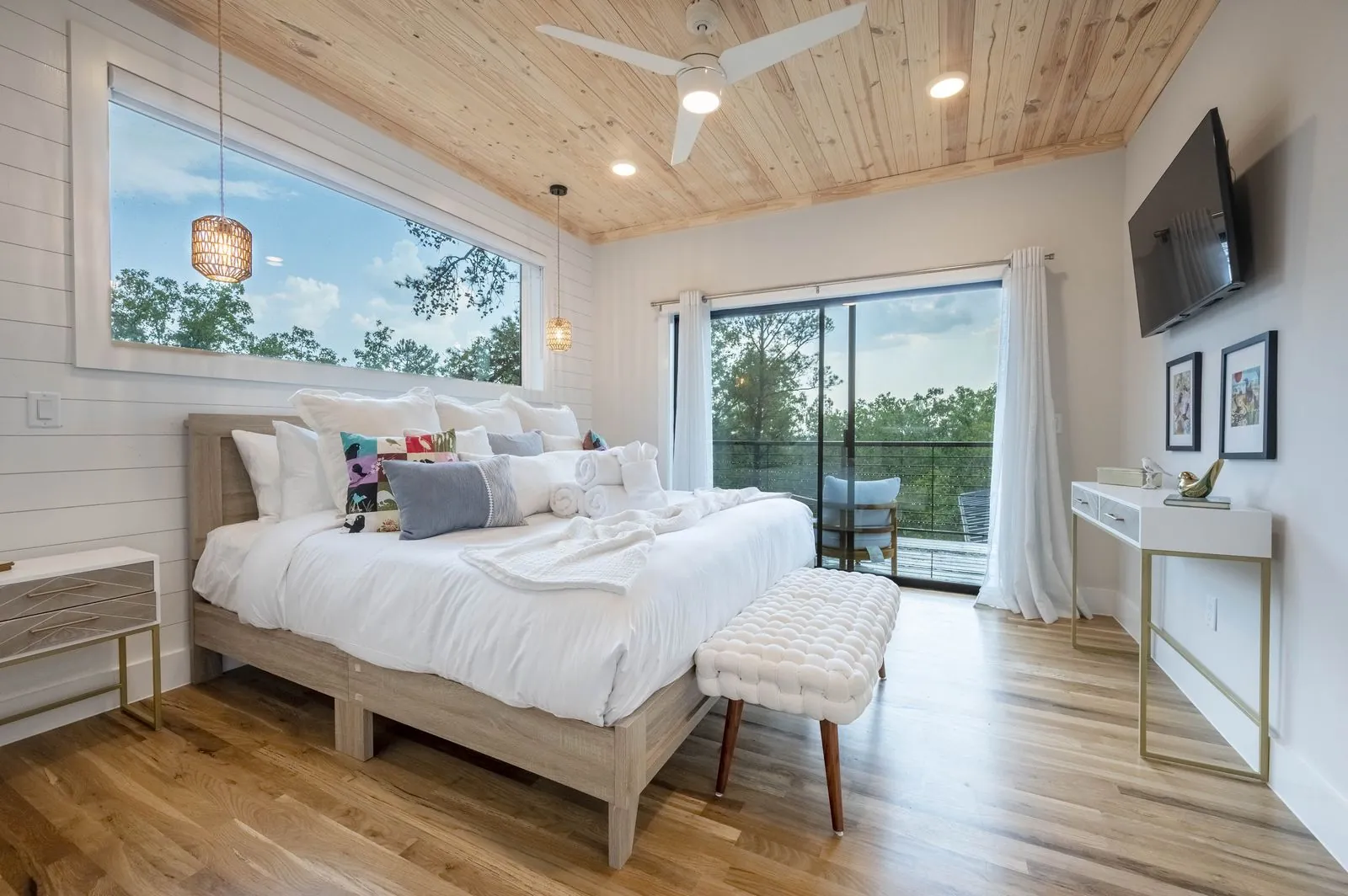 Bedroom at The Aroha with king bed, wood-paneled ceiling, pendant light, and large forest-view window