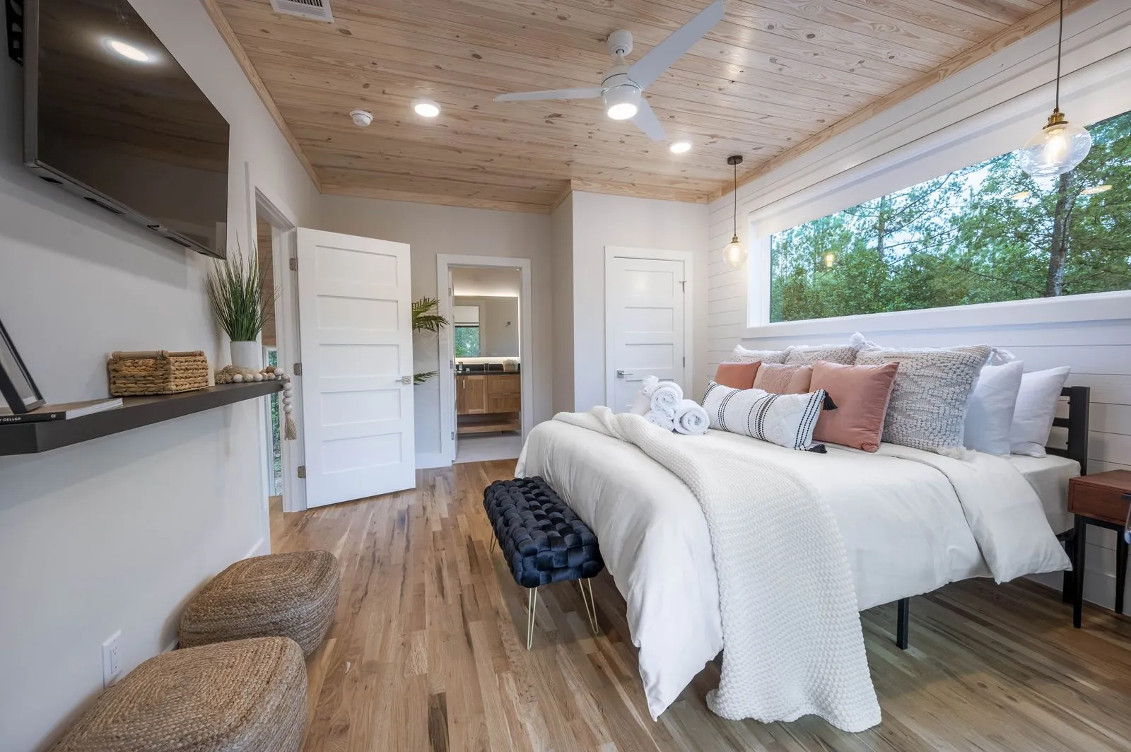 King suite at The Aroha with white bedding, blue accent pillows, wicker pendants, and forest views