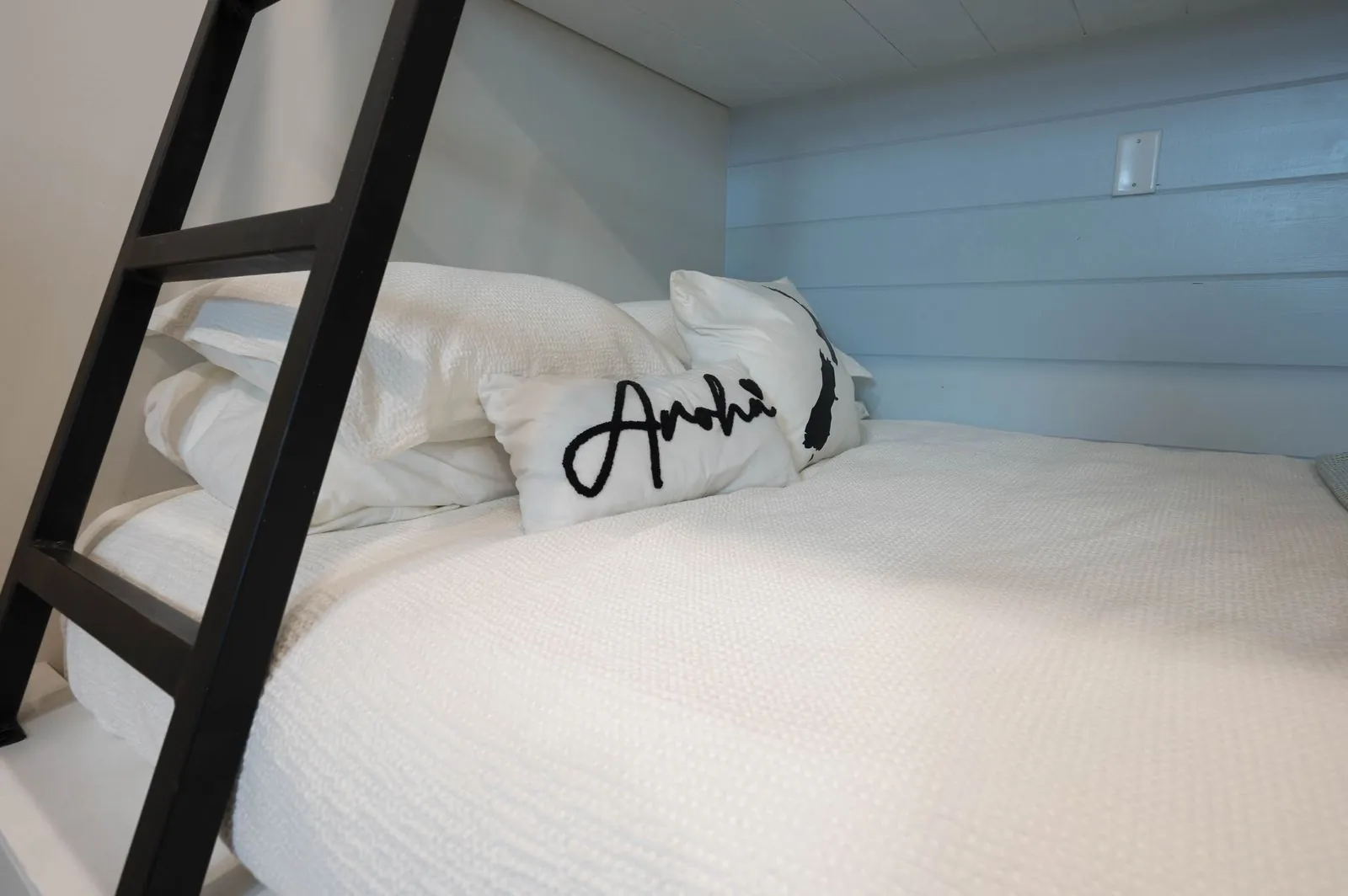 Bedroom at The Aroha with wood ceiling, king bed, white bedding, and blue accent pillows