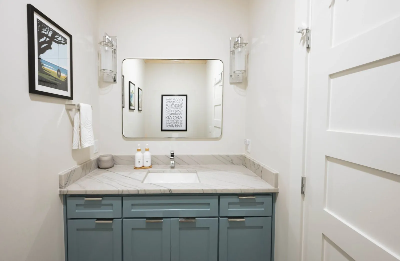 Bunk room bathroom at The Aroha with gold-framed round mirror, white vanity, and potted plant