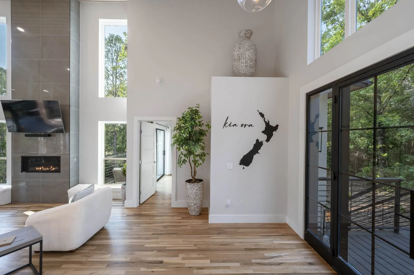 Living room at The Aroha with linear fireplace, white sofas, and panoramic forest views through large windows