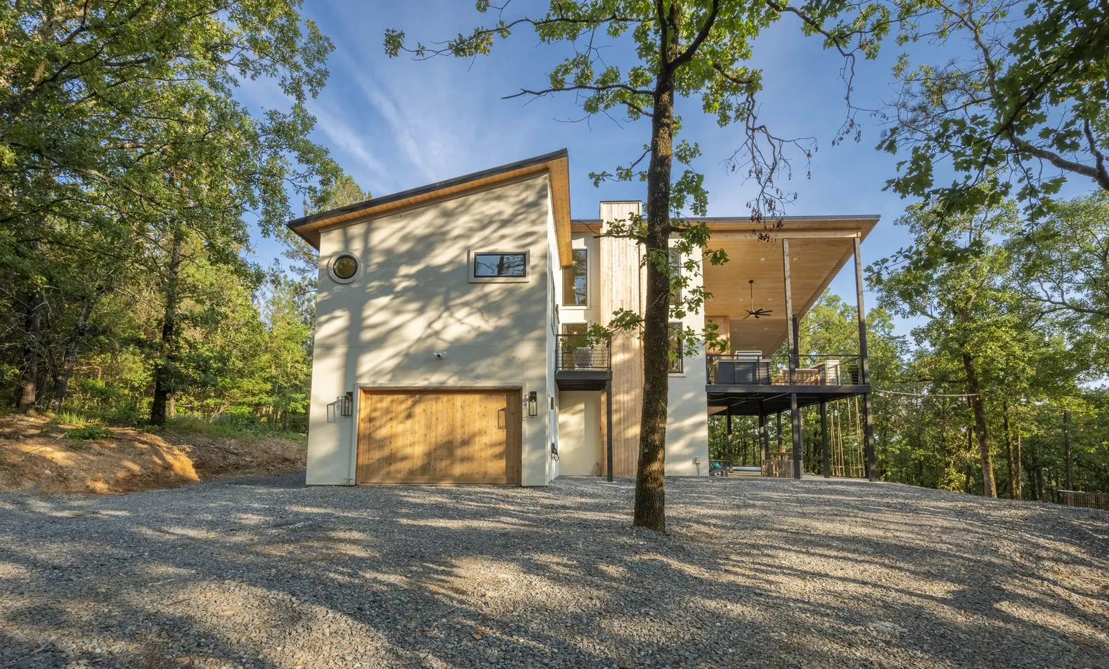 Front exterior of The Aroha at dusk with garage, multi-level decks, and forest setting