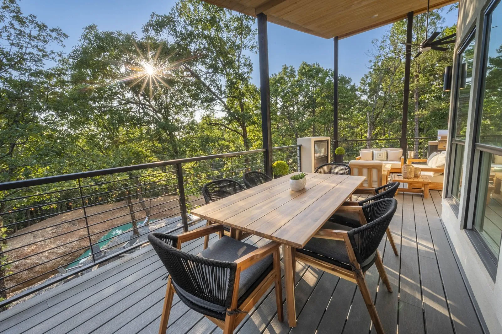 Covered deck at The Aroha with teak lounge furniture, outdoor fireplace, and grill at sunset