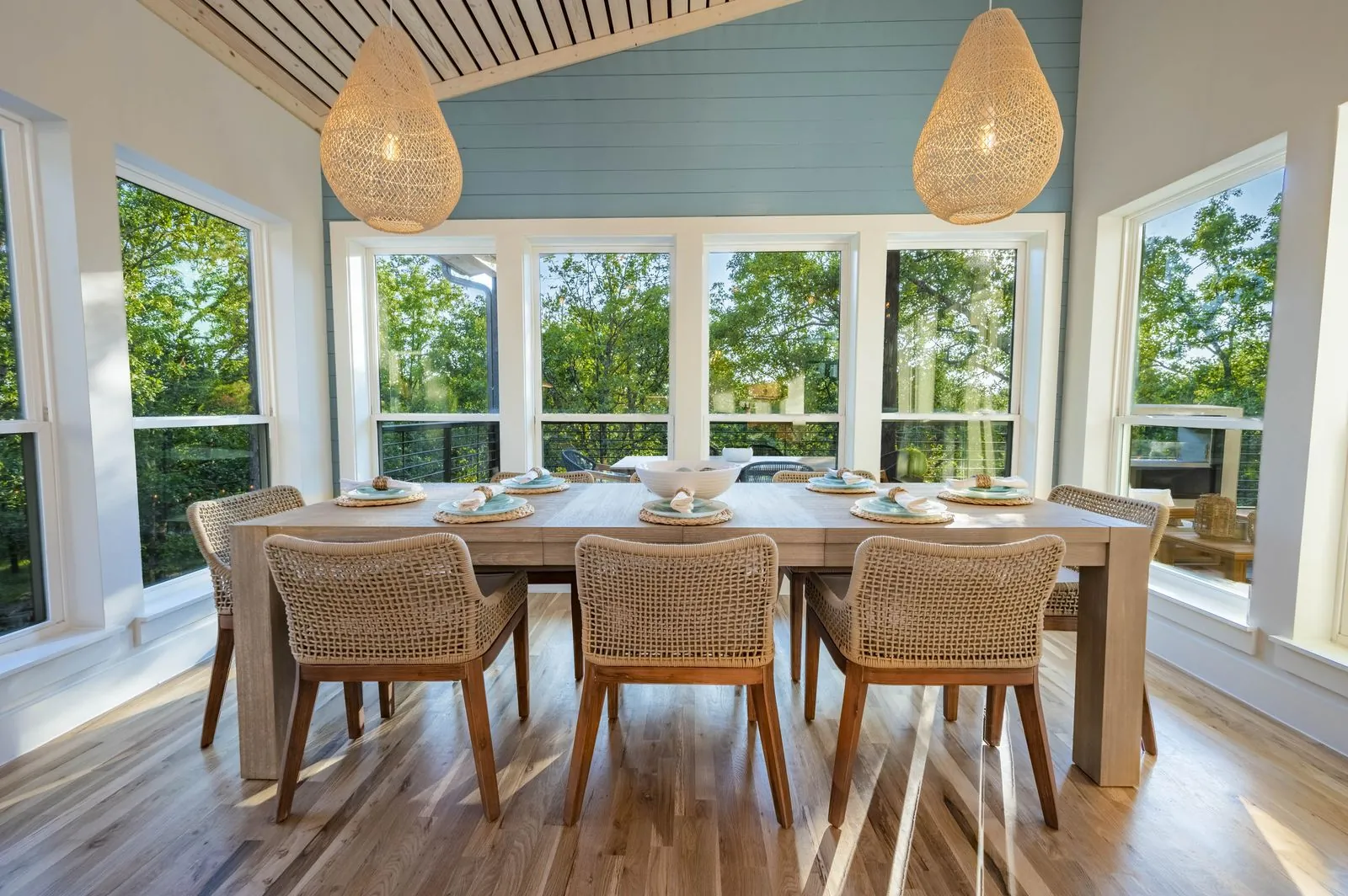 Dining table set with teal place settings and wicker chairs at The Aroha with panoramic forest views