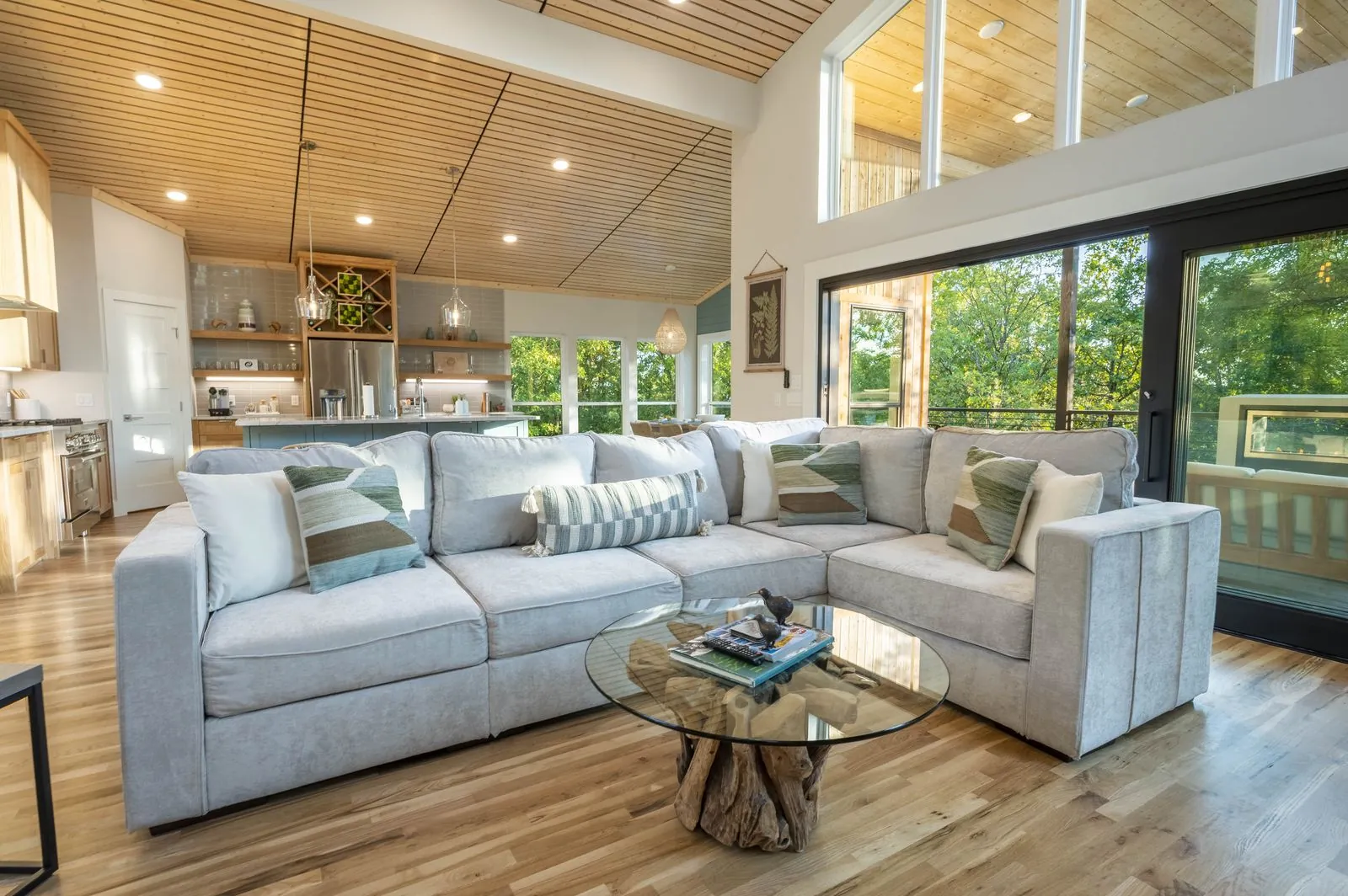 Living room at The Aroha with white sectional, slatted wood ceiling, and large forest-view windows