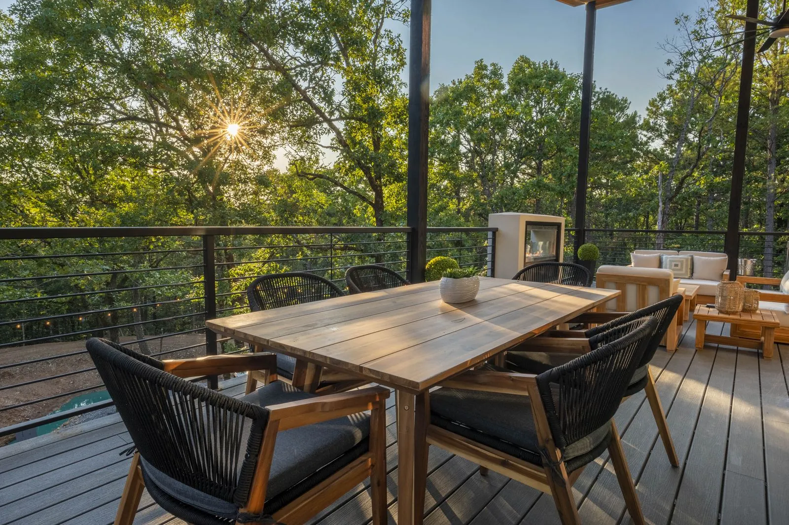 Outdoor dining area at The Aroha with black woven chairs, wood table, and sunset forest views