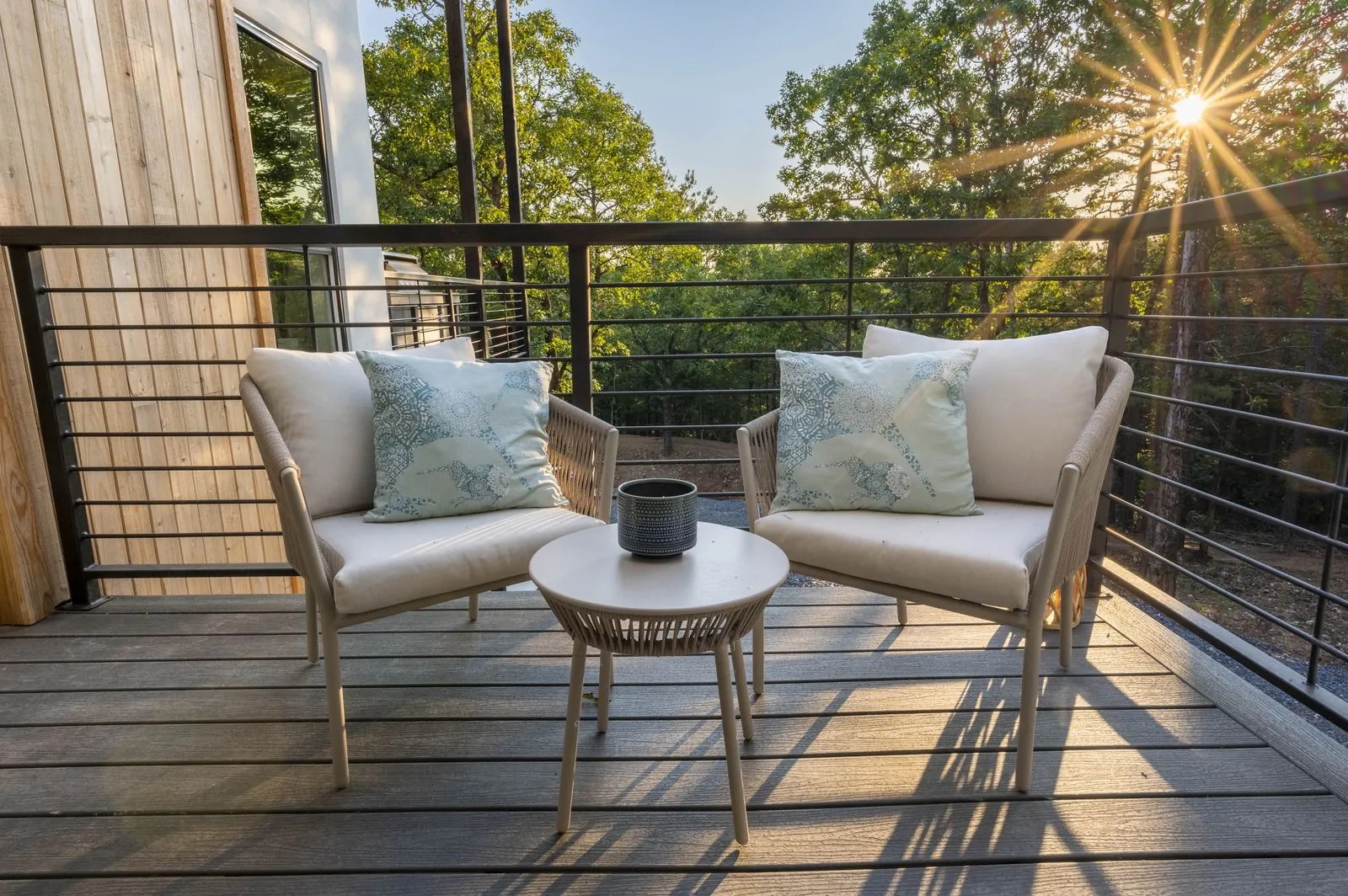 Balcony seating at The Aroha with wicker bistro chairs and cable railing overlooking the forest