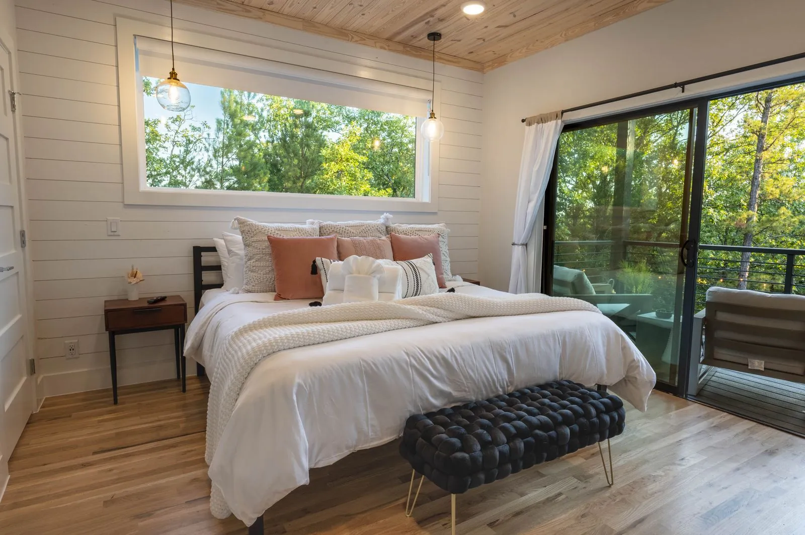 King bedroom at The Aroha with pink accent pillows, navy velvet bench, and balcony view