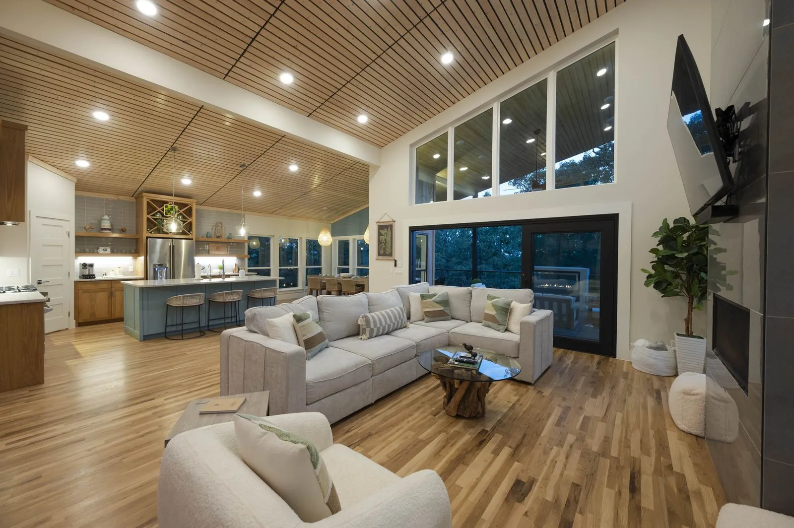 Covered deck outdoor living area at The Aroha with teak sofas, grill, and outdoor fireplace at sunset