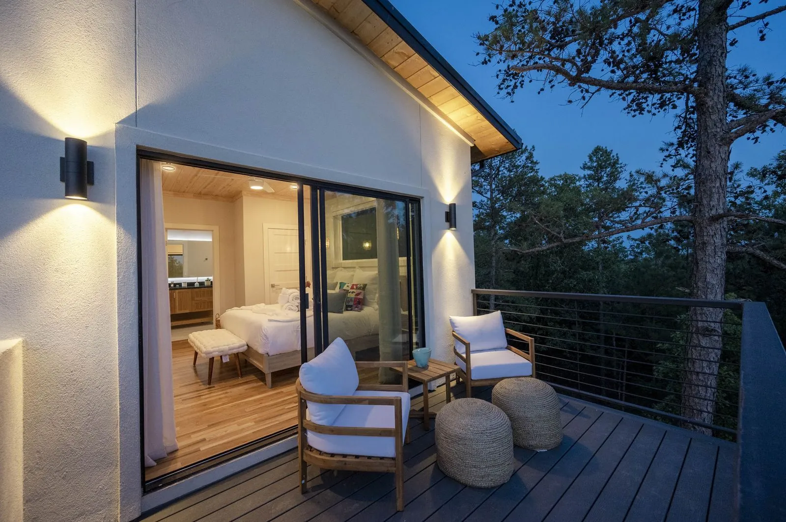 Hot tub and sun loungers at The Aroha deck with forest canopy and string lights at sunset