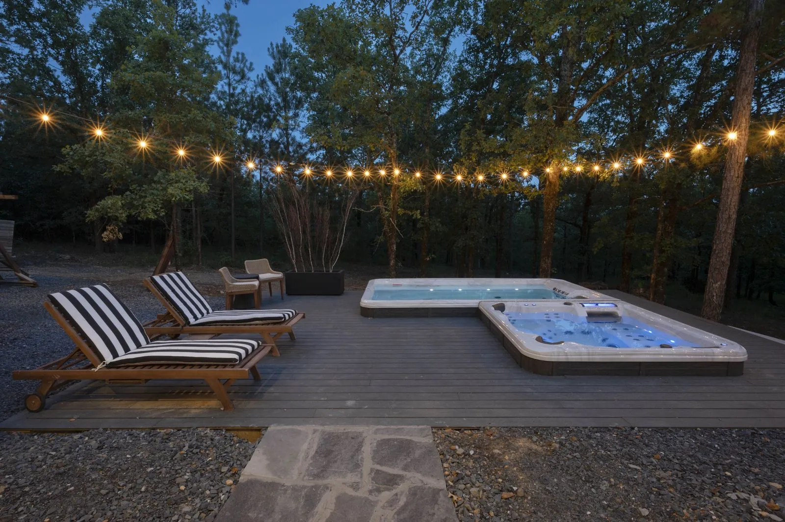 Covered deck with teak furniture at The Aroha at night with string lights and hot tub glow below