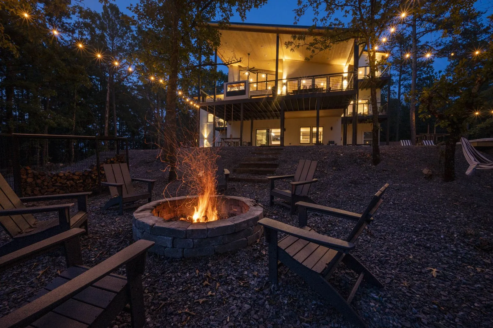Fire pit at night with string lights and Adirondack chairs at The Aroha