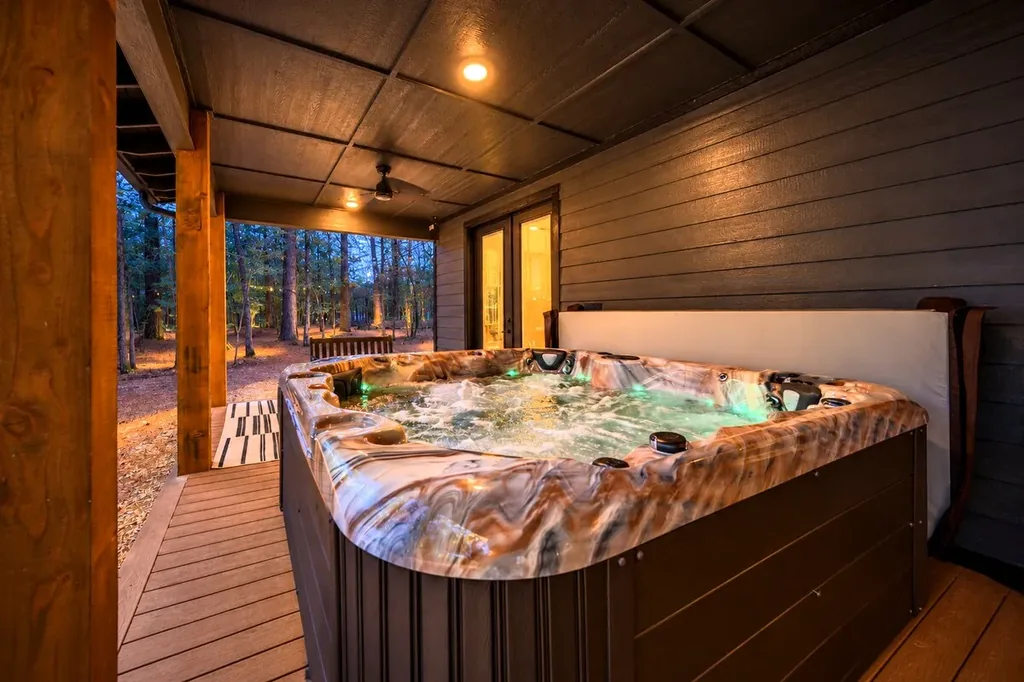 The Black-Beary — A private hot tub bubbles on the covered back deck, surrounded by trees. Glass doors lead directly inside from the deck.