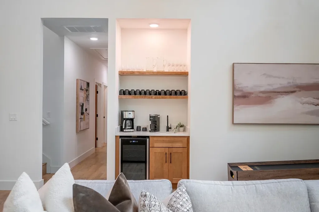 The Black-Beary — A built-in nook off the living room holds a coffee maker, espresso machine, sink, and wine fridge, with mugs and glassware stocked on open shelving above.