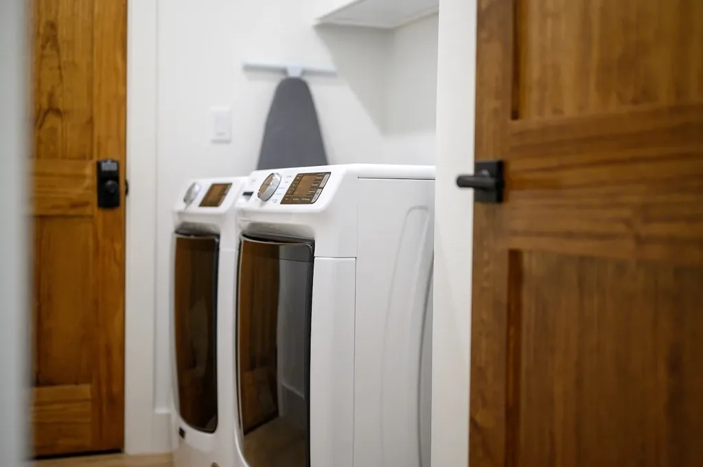 The Black-Beary — A private laundry closet with a full-size front-load washer and dryer, plus an ironing board for pressing clothes.