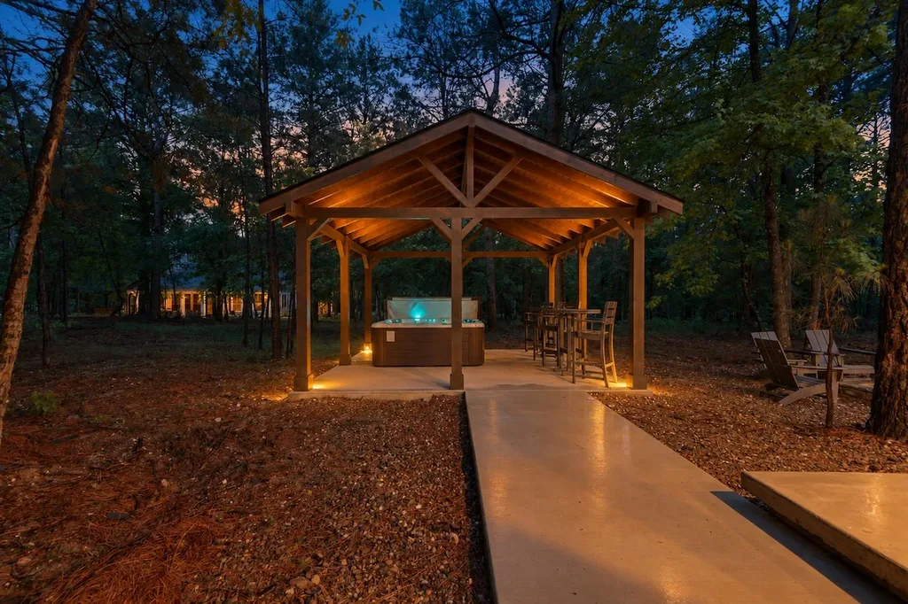 A private wood-frame cabana at the cabin shelters a hot tub and a seating area, lit for evening use among the trees.
