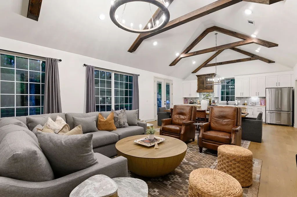 The living area features a vaulted ceiling with exposed wood beams, a sectional sofa, leather armchairs, and an open view into the gourmet kitchen.