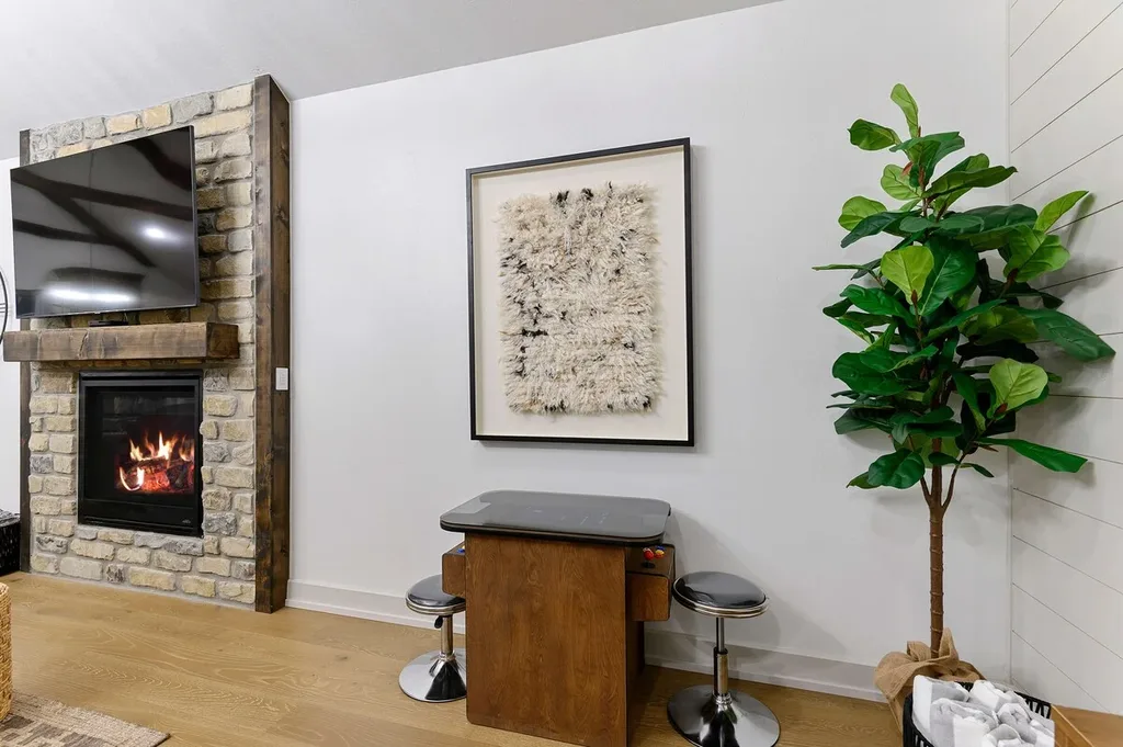 The living area has a stone gas fireplace below a mounted smart TV and a two-seat tabletop arcade game against the wall.