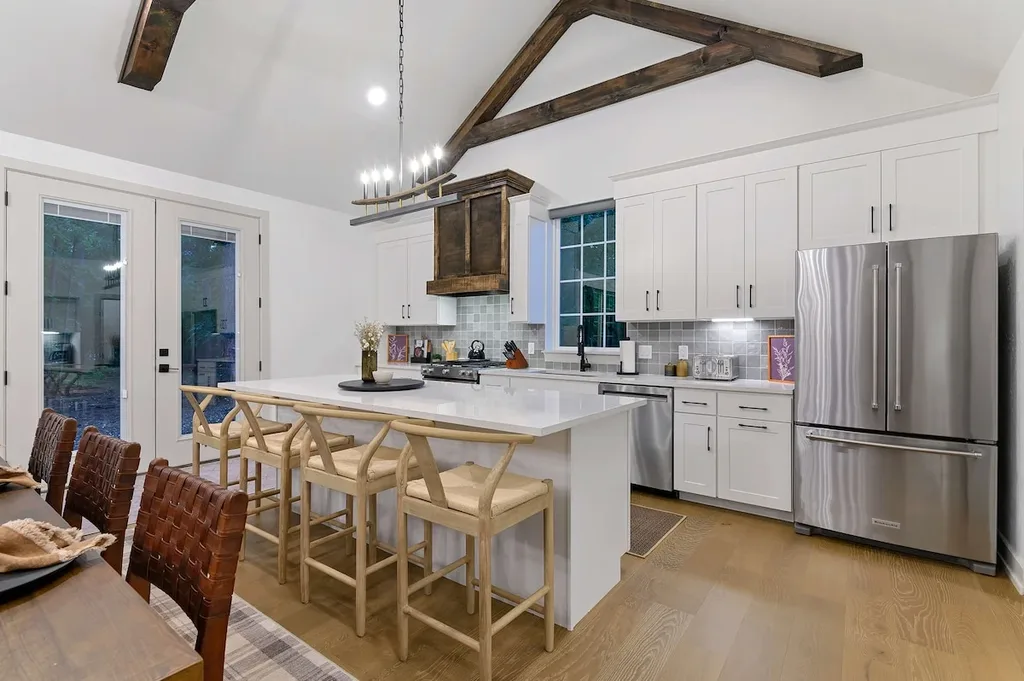The private gourmet kitchen features a stainless steel refrigerator and gas range, a large island with seating for four, and a vaulted ceiling with exposed wood beams.