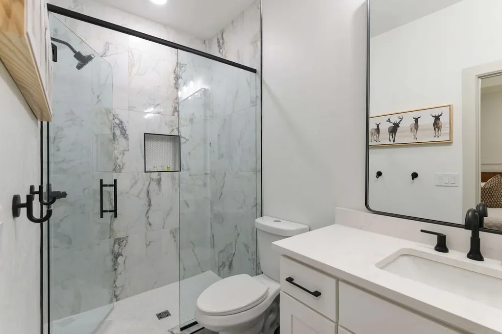 This private ensuite bathroom has a walk-in glass shower with marble tile surround and a vanity with quartz countertop.