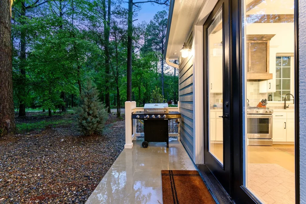 The covered back patio has a private BBQ grill and opens straight into the gourmet kitchen through glass doors, with wooded views beyond.