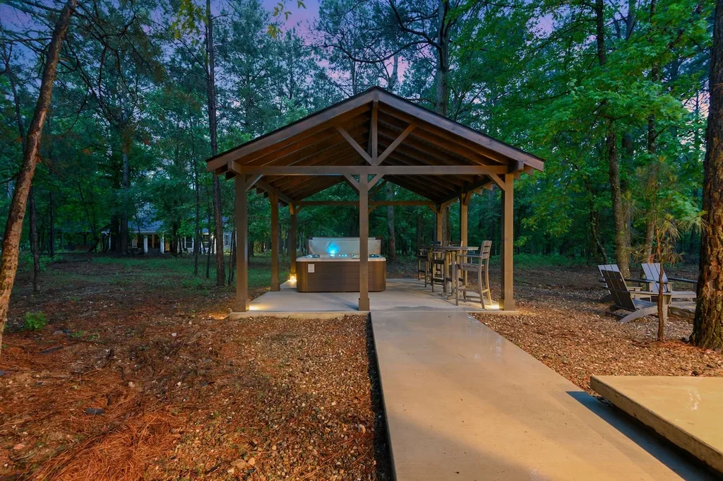 A private, covered cabana at the cabin houses the hot tub and a high-top seating area, set among the trees along a lit concrete path.