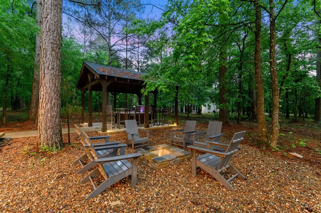 A private fire pit with six Adirondack chairs sits in the wooded backyard, steps from the covered patio and hot tub cabana.