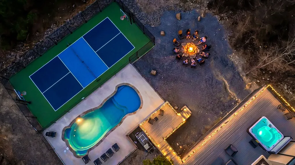 Aerial drone view of The Jade showing private pickleball court, heated pool, hot tub, and outdoor fire pit nestled among pine trees