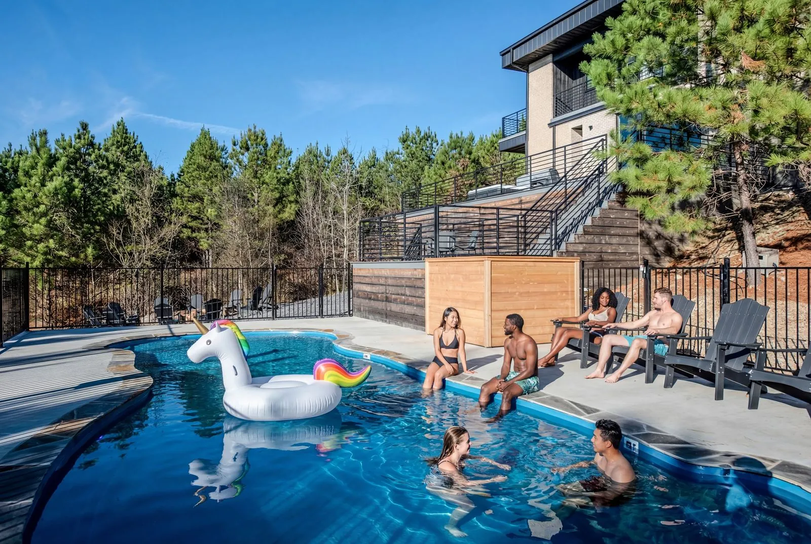 Guests enjoying the heated outdoor pool at The Jade with pool floats, multi-level deck, and surrounding pine forest