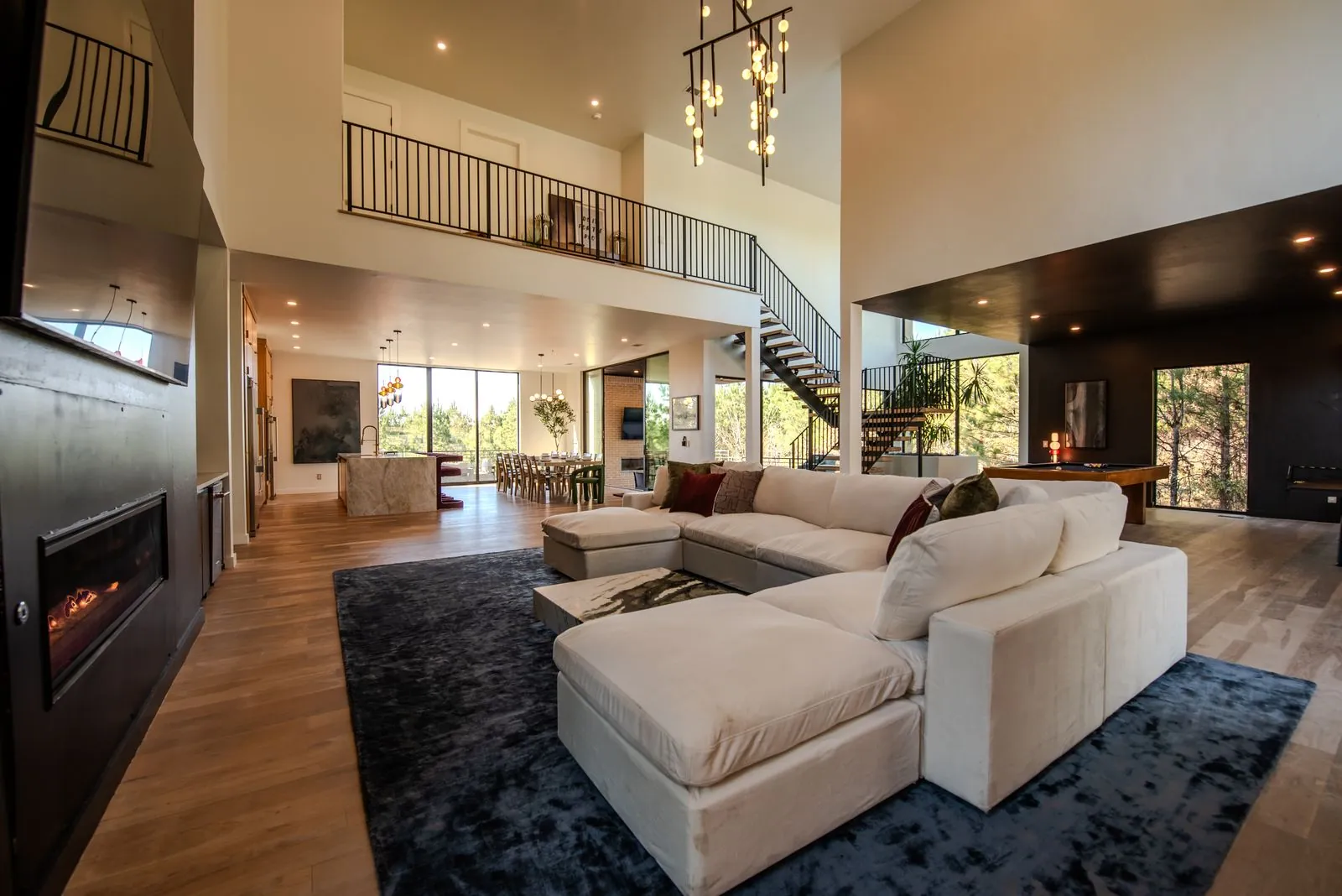 Open-concept great room at The Jade with vaulted ceilings, spiral staircase, designer chandelier, and plush white sectional