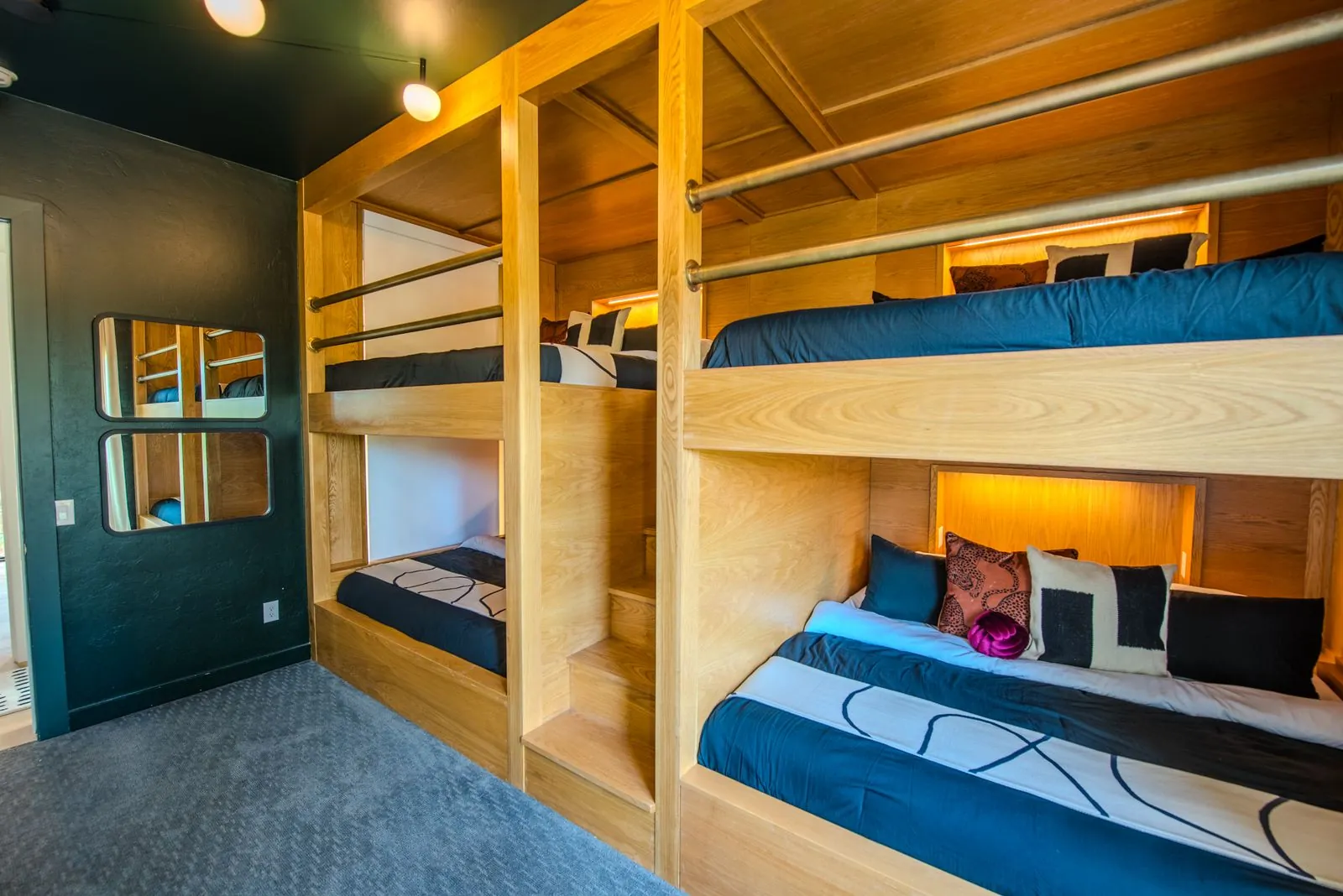 Built-in wooden bunk beds with warm accent lighting, dark navy bedding, and individual reading nooks at The Jade