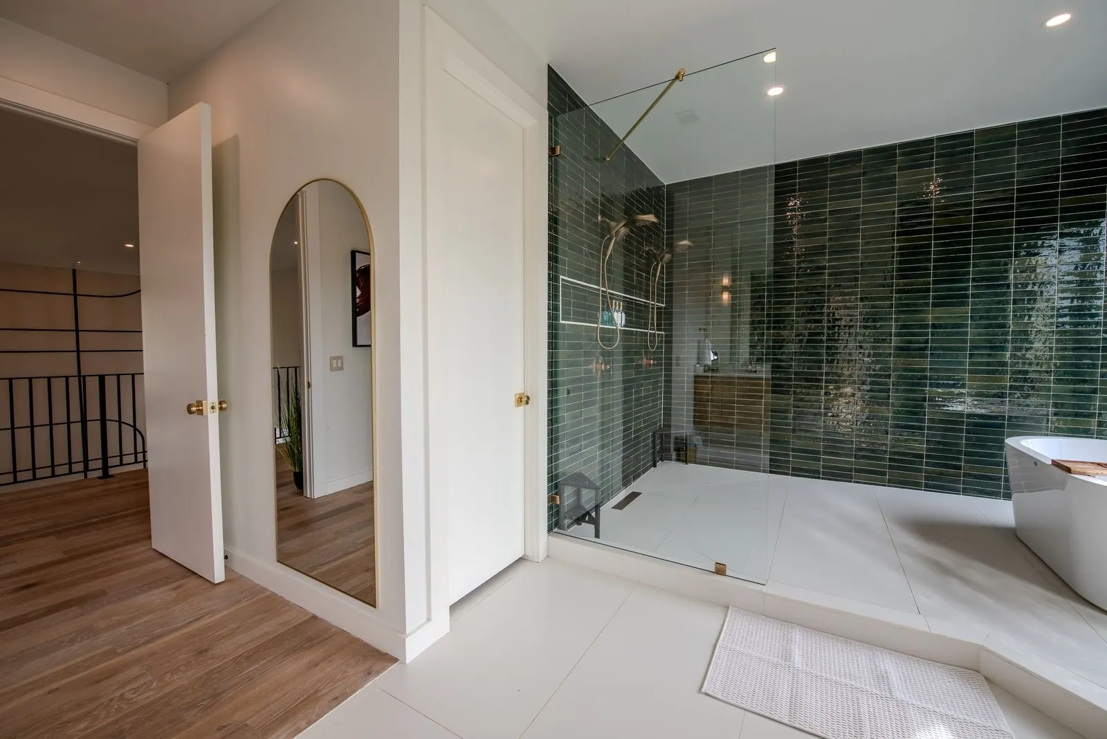Green-tiled master bathroom at The Jade with glass-enclosed shower, freestanding tub, and natural light from large windows