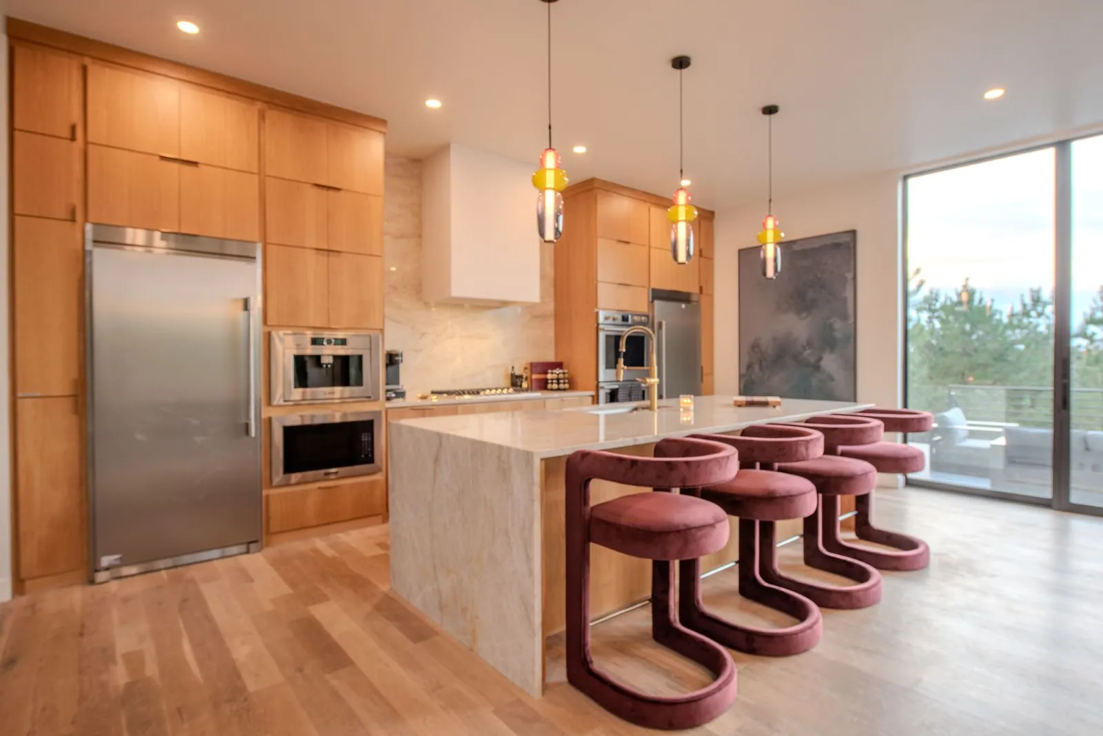 Gourmet kitchen at The Jade with marble waterfall island, velvet burgundy bar stools, colorful pendant lights, and stainless appliances