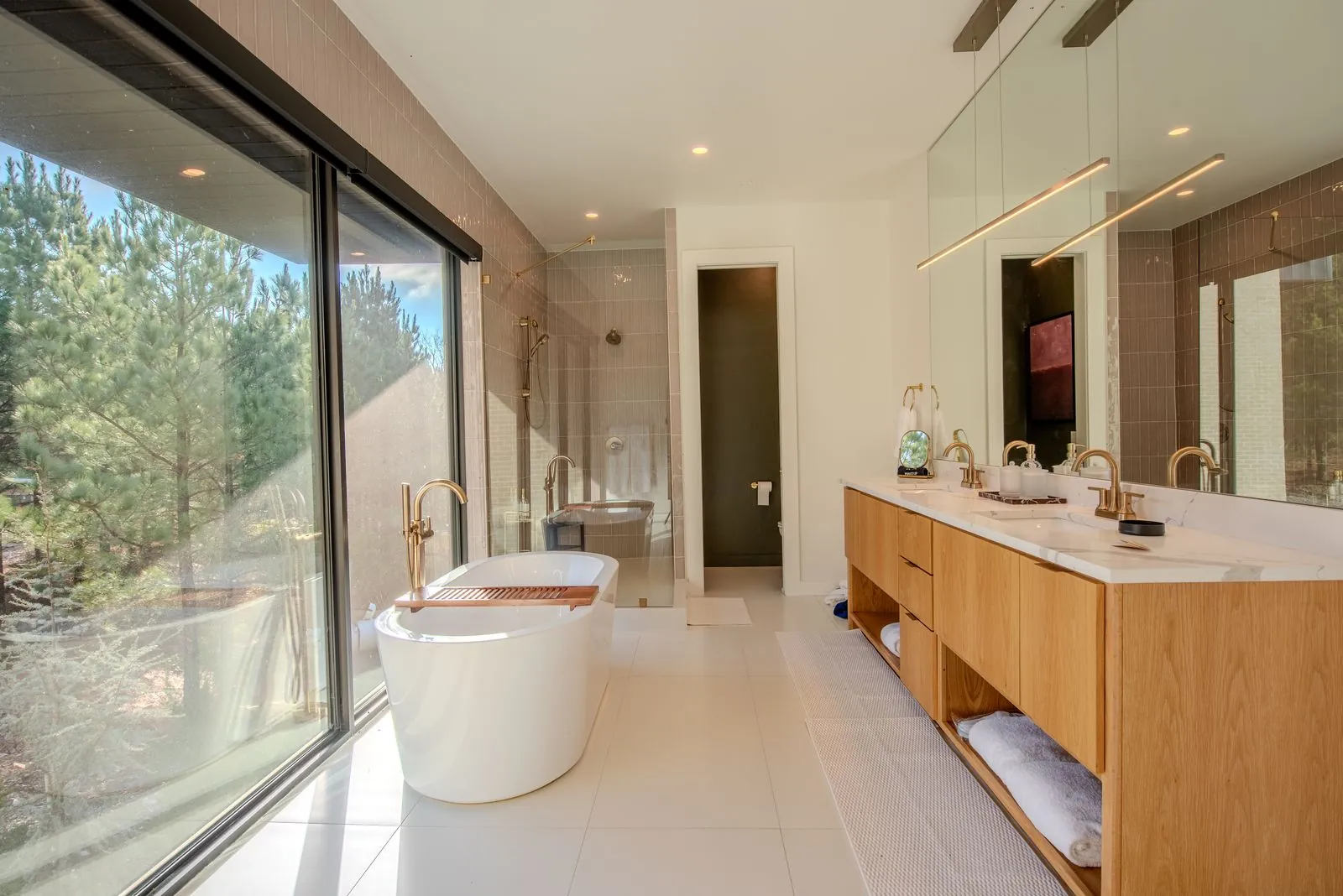 Luxury bathroom at The Jade with freestanding white tub, green tile accent wall, and panoramic window overlooking autumn trees
