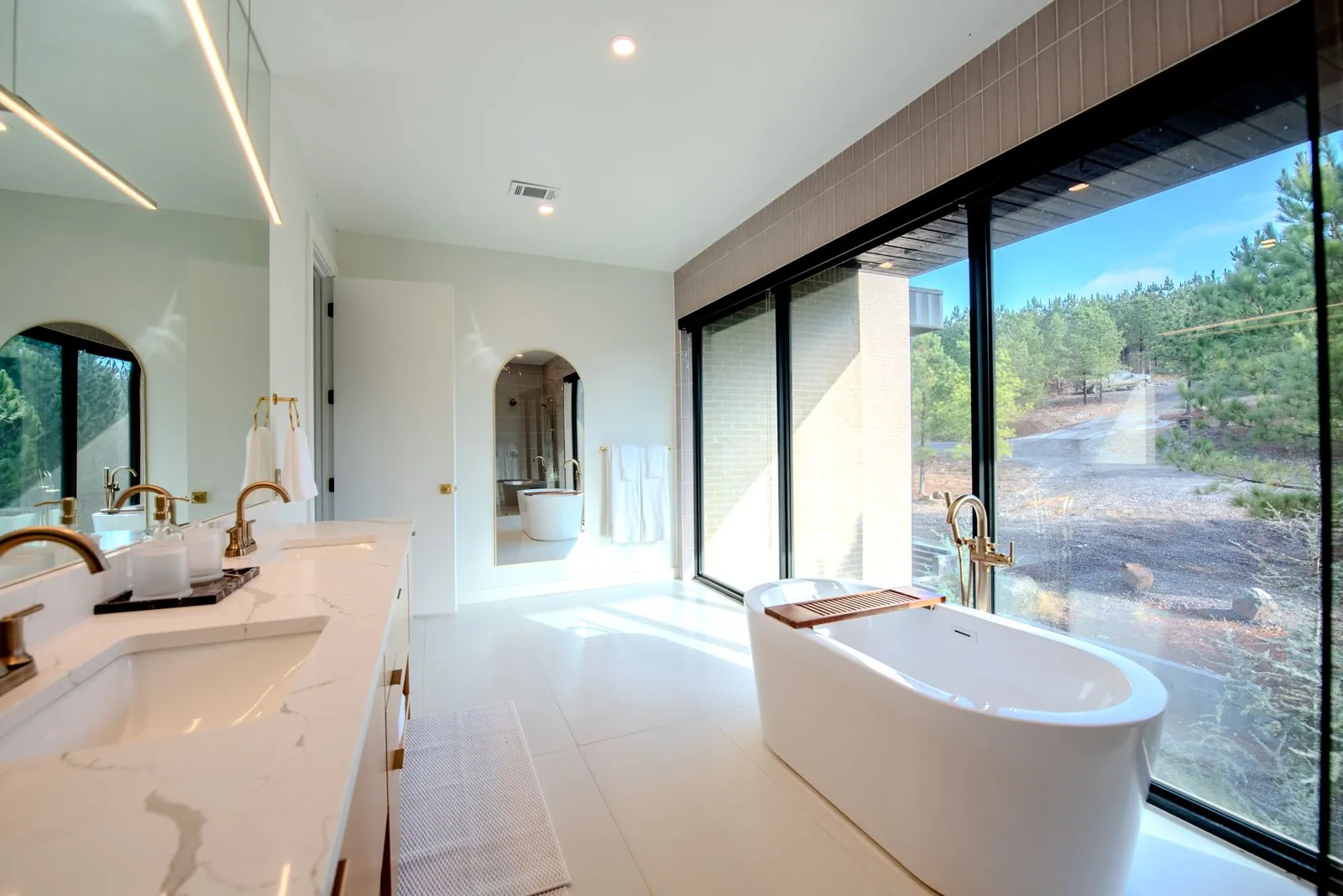 Spa-inspired freestanding soaking tub in green mosaic-tiled bathroom with floor-to-ceiling window and forest view at The Jade