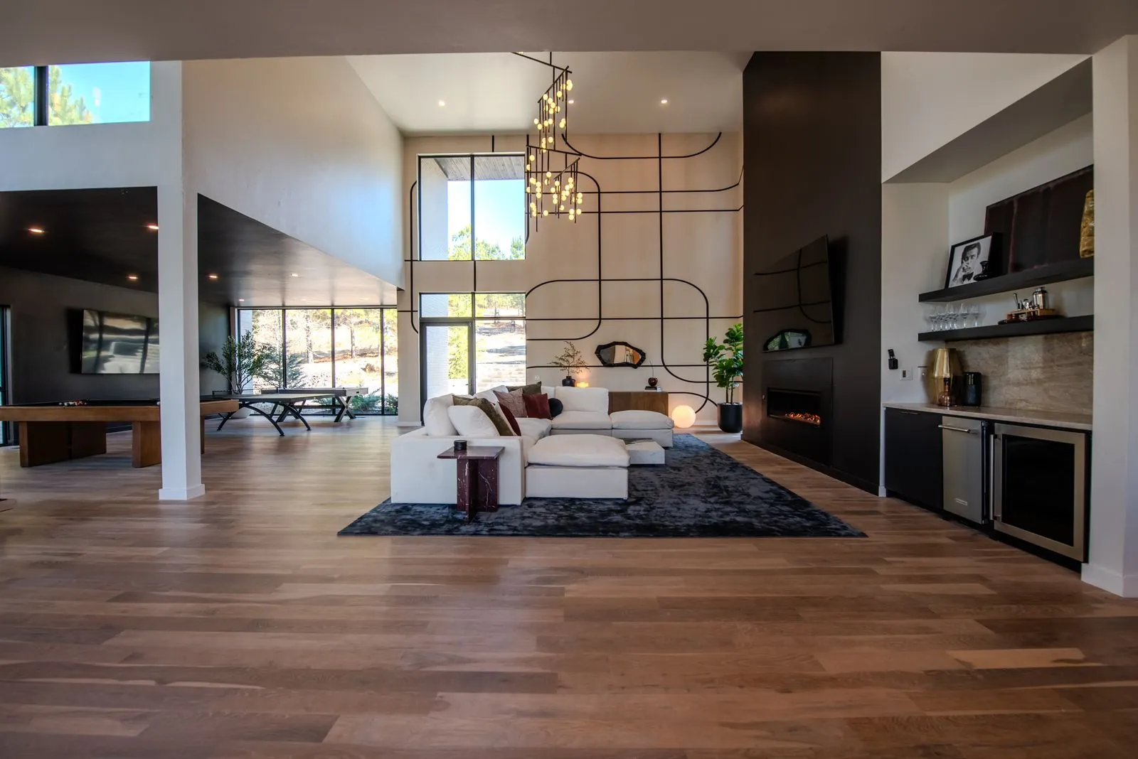 The Jade great room with white sectional, linear fireplace, entertainment wall, and floor-to-ceiling windows with forest views