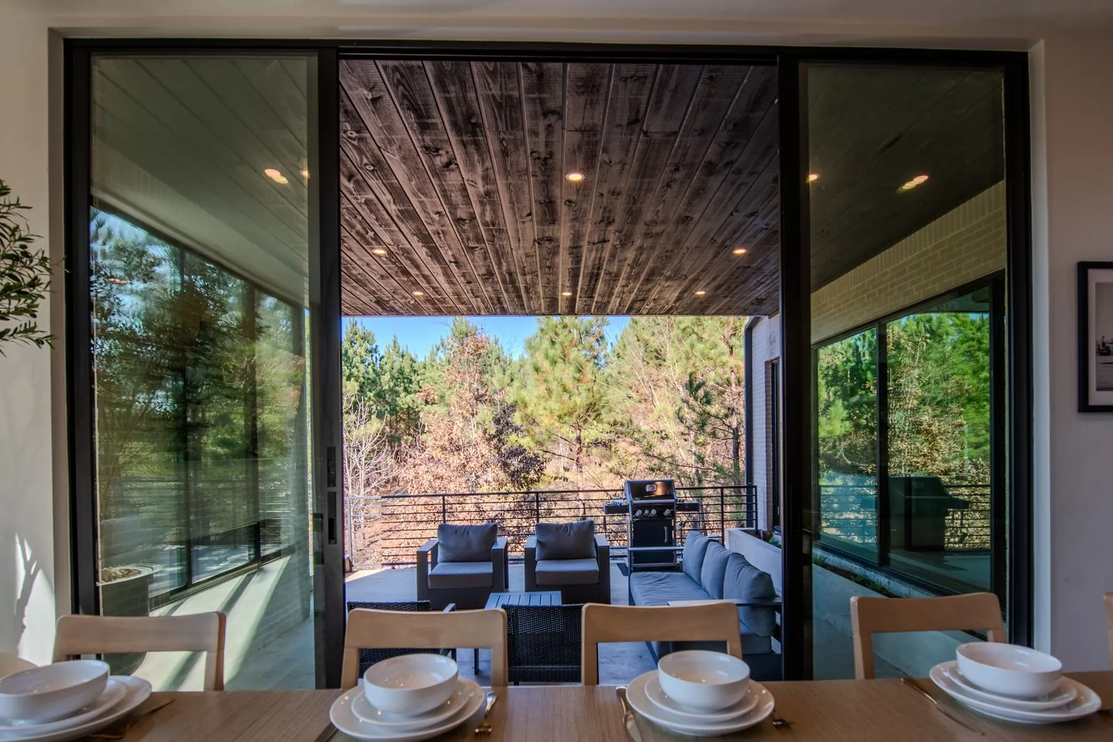 Elegant dining table with place settings and pendant chandelier framed by large windows with pine tree views at The Jade