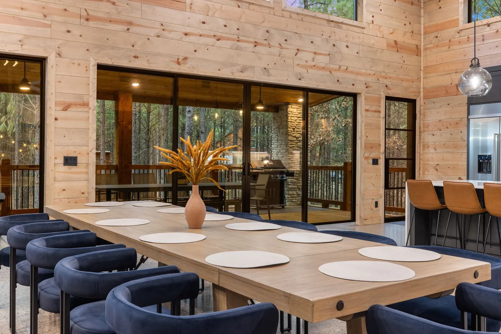 Full dining room at LivNLove with long table, navy chairs, floor-to-ceiling windows, and overhead chandelier