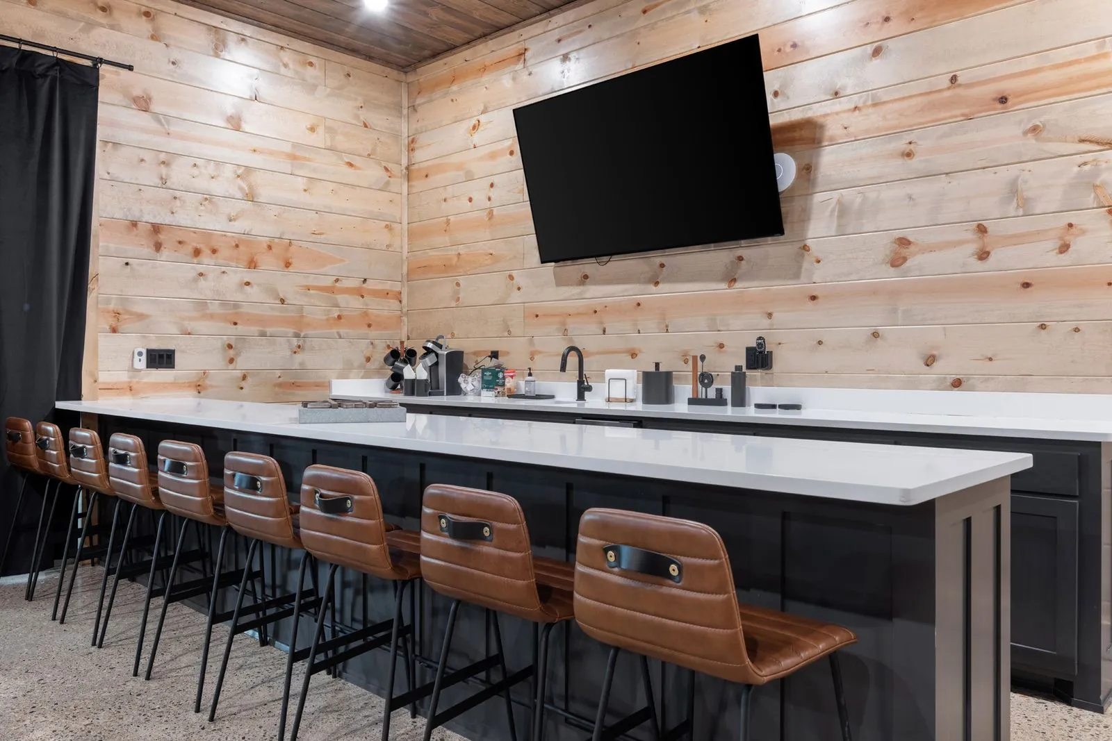 Wall-mounted flat screen TV on wood-paneled wall with bar seating area below at LivNLove upper level