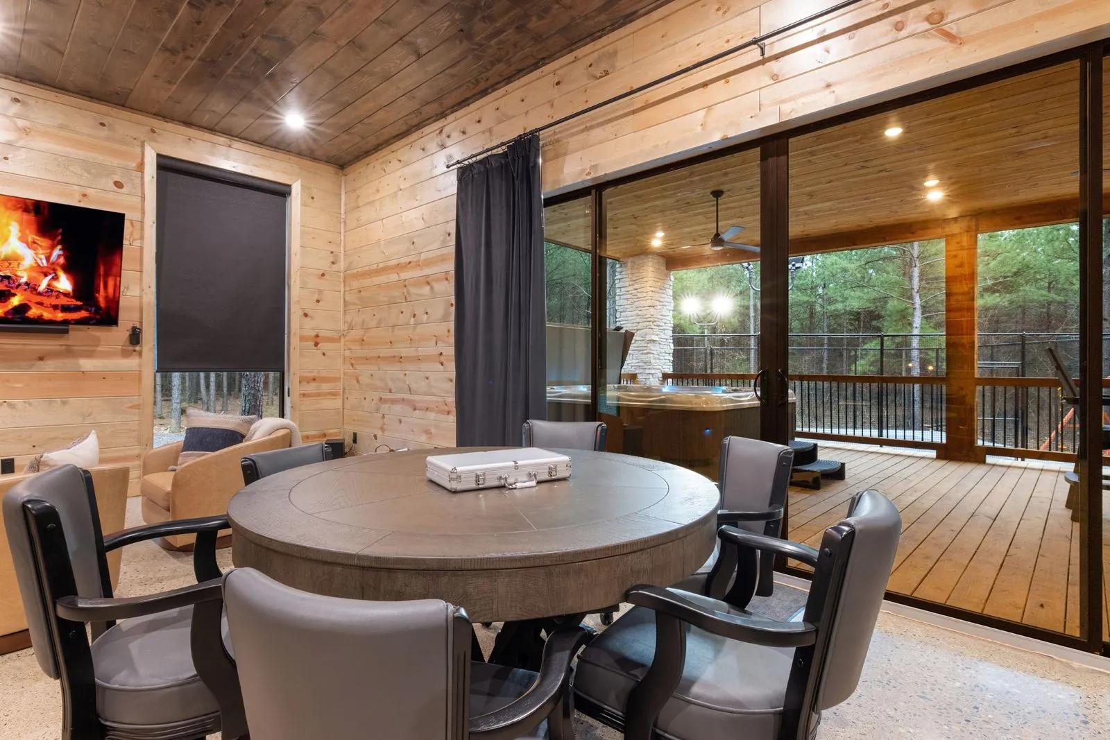 Lounge area at LivNLove with leather swivel chairs, fireplace, dark curtains, and forest views through windows