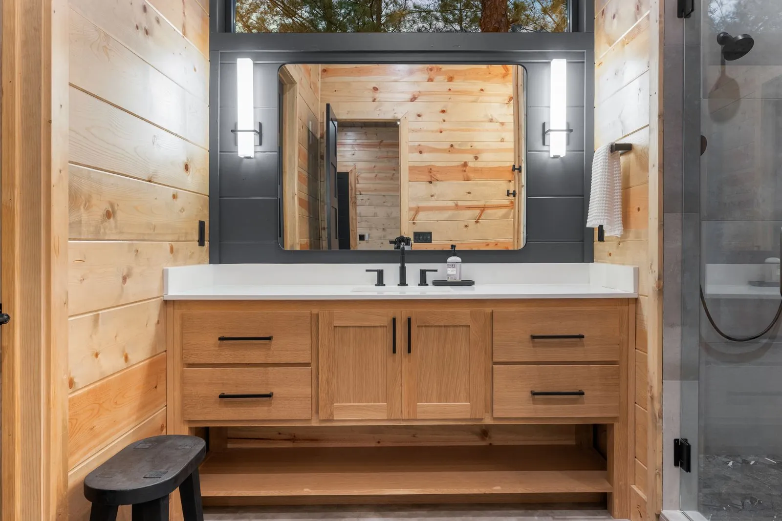 Freestanding oval soaking tub with window view of forest, wood-paneled walls, and mirror at LivNLove