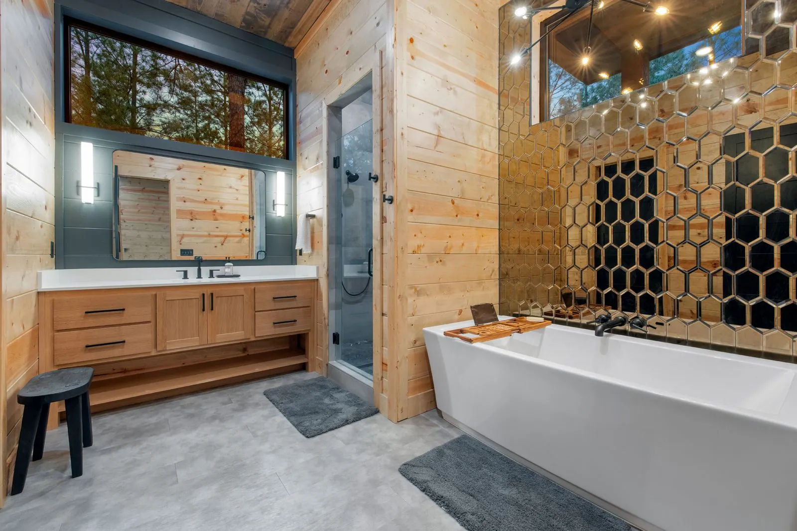 Freestanding bathtub with honeycomb hexagonal wall art, wood surround, and vanity mirror at LivNLove