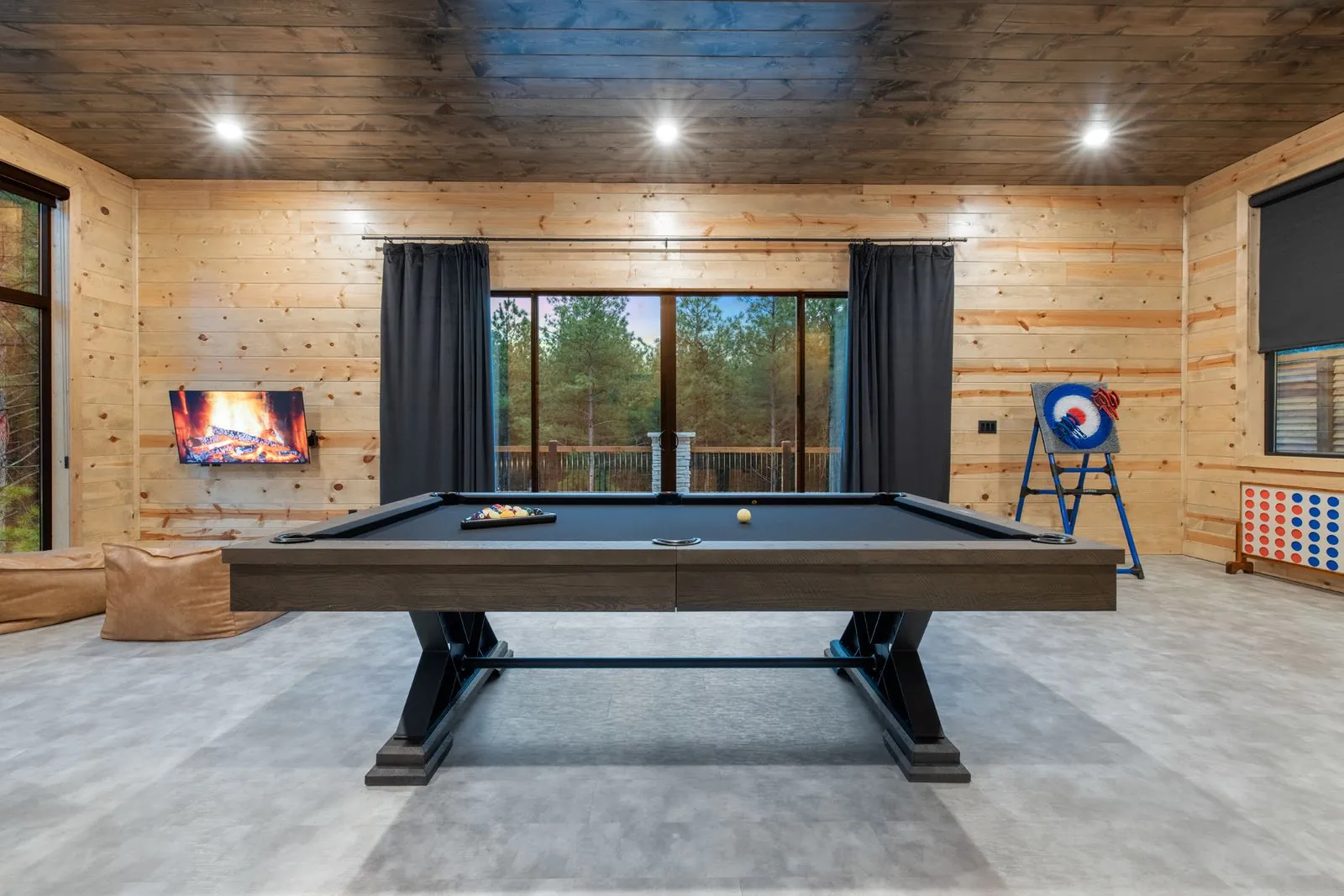 Pool table room at LivNLove with dark blue walls, recessed lighting, and forest views through windows