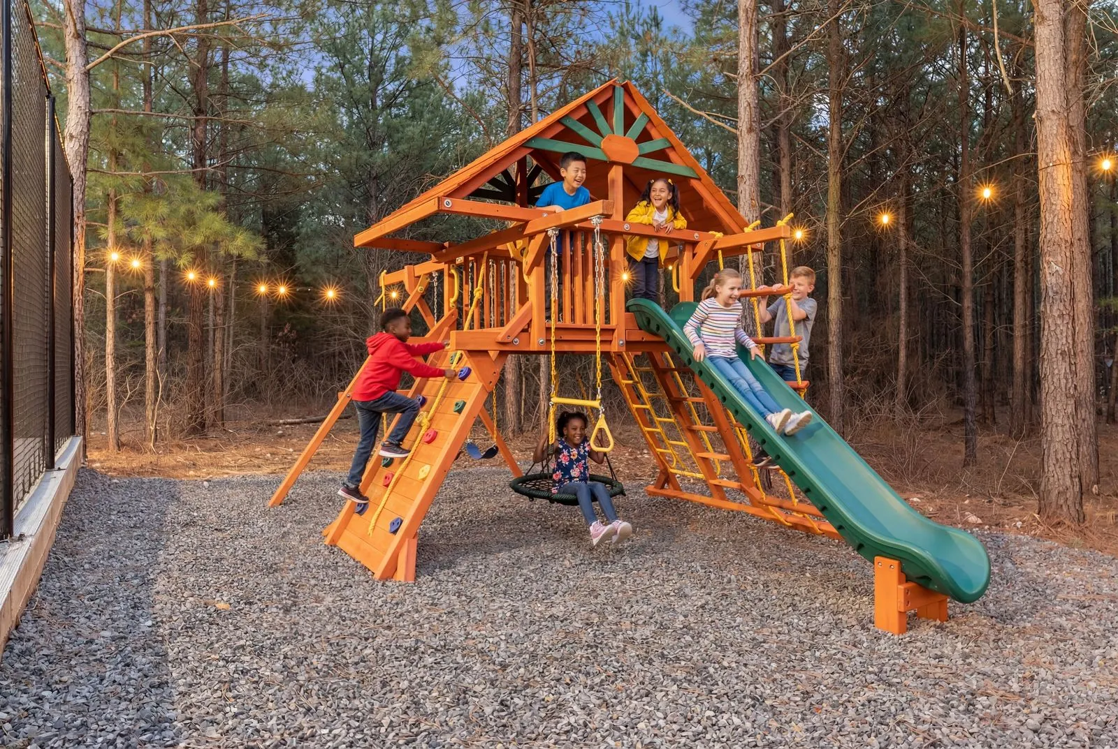 Children playing on the wooden playground with slide and climbing structure among pine trees at LivNLove