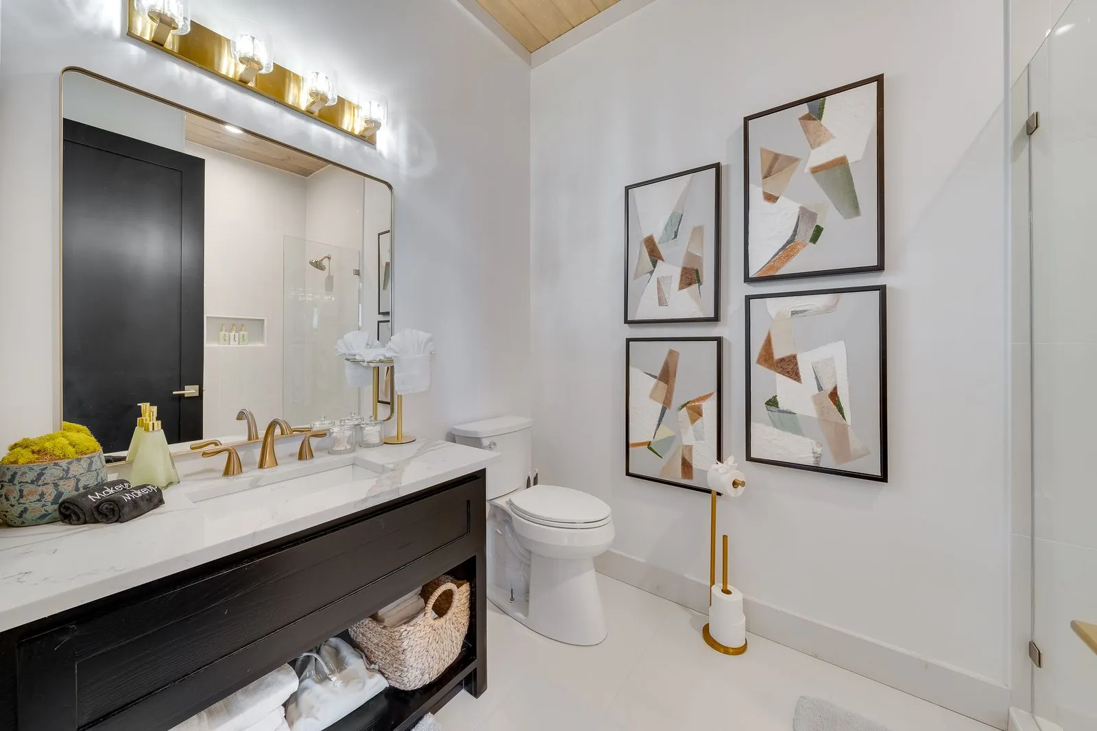 Double vanity bathroom at The Malibu with oval mirrors, gold light fixtures, dark cabinets, and fresh flowers